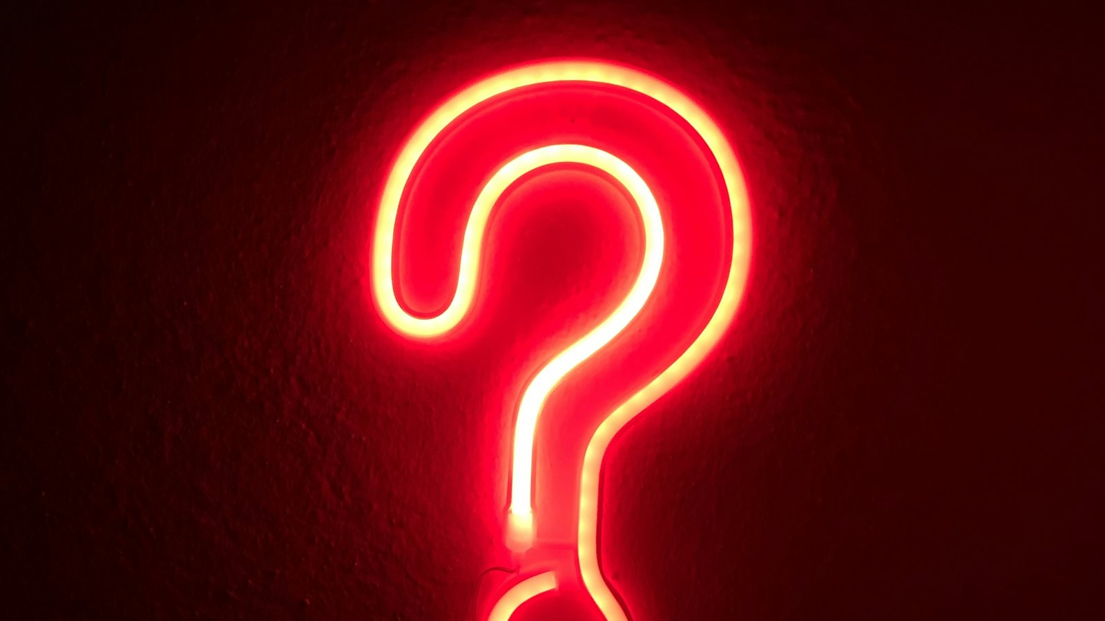 A red neon question mark on a wall