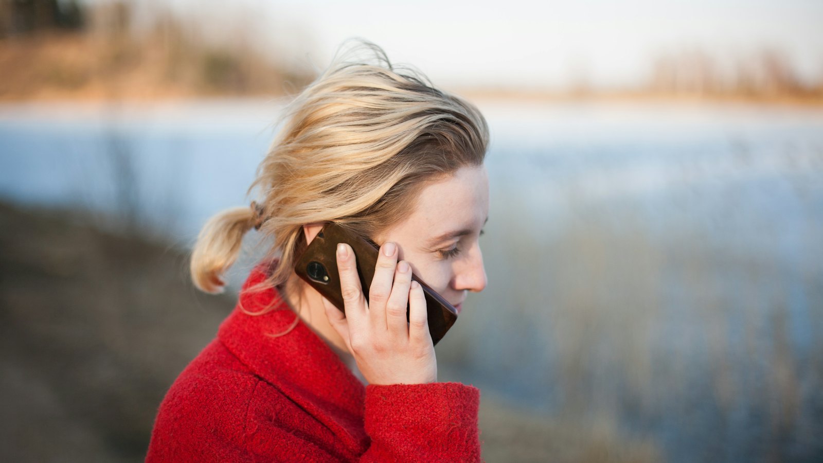 A woman listening to her phone by a lake