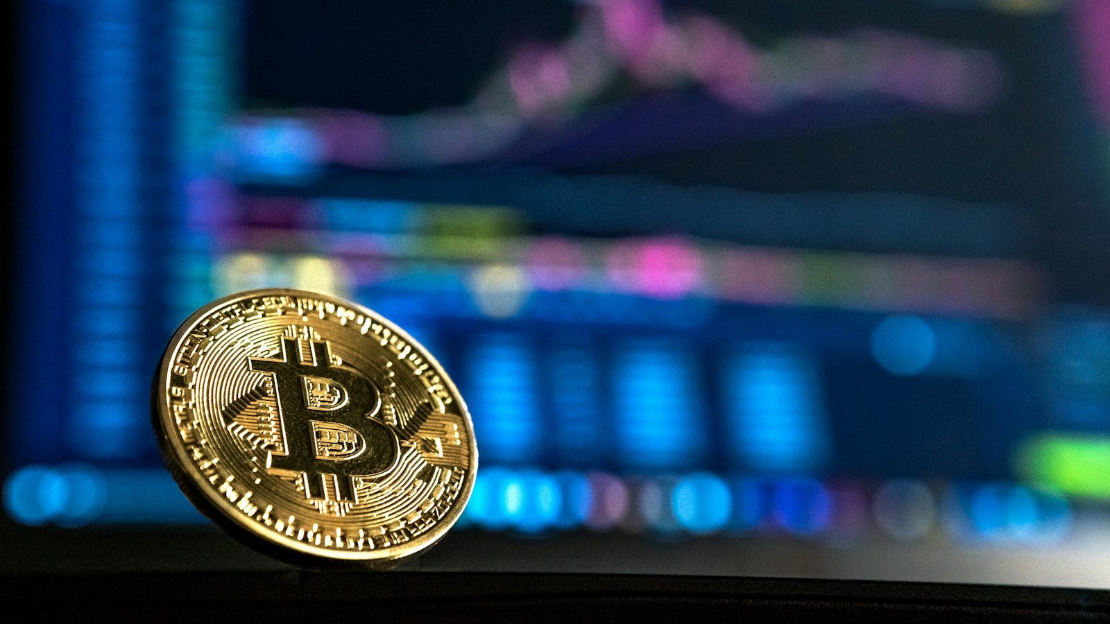 A gold Bitcoin coin standing in front of a blurred trading chart
