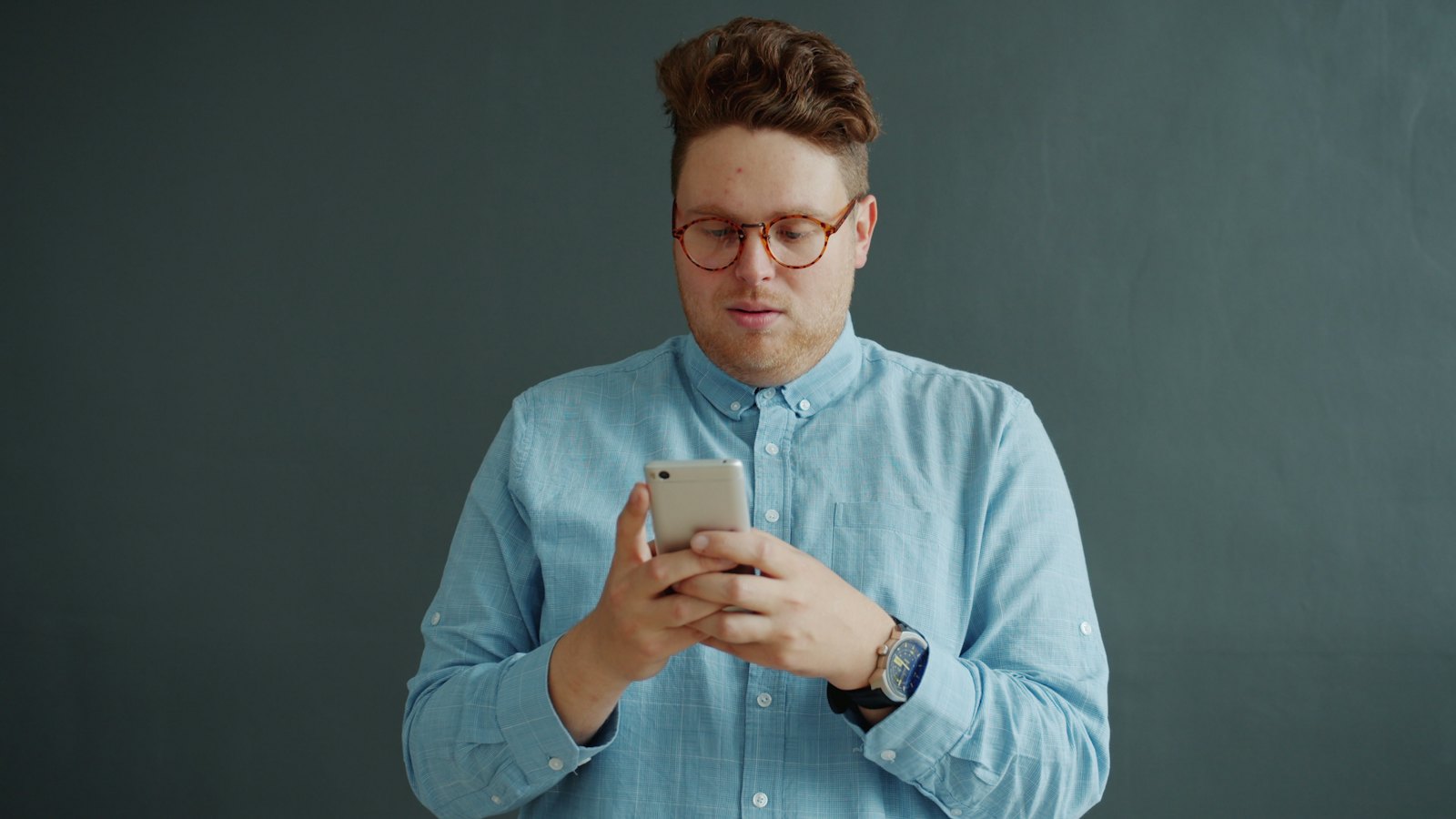A man in glasses and a blue shirt looking closely at his phone