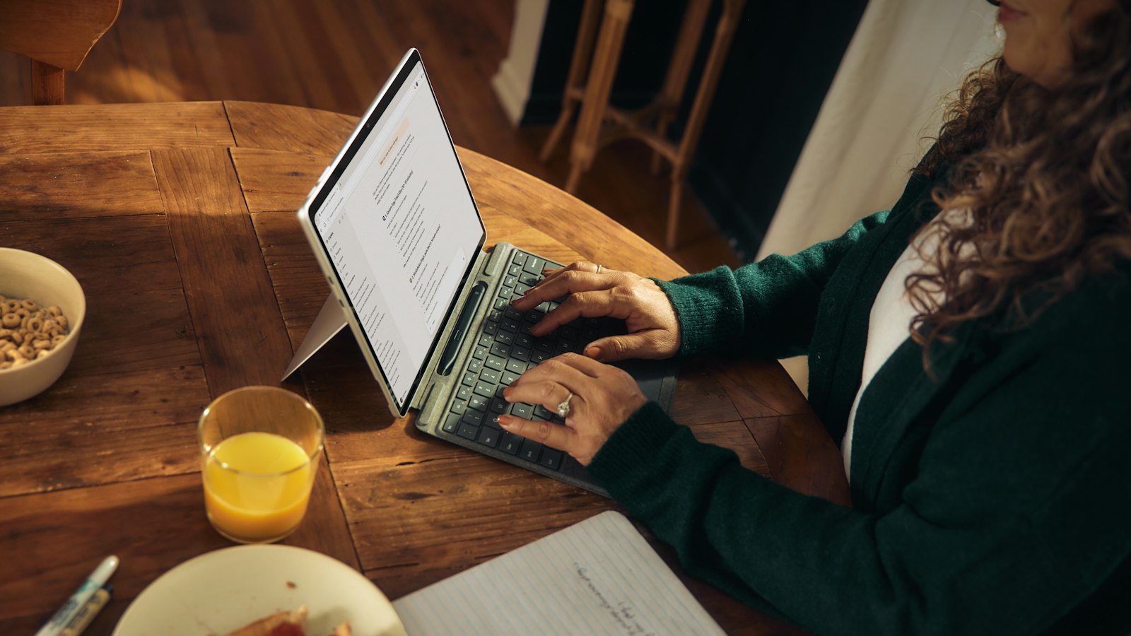 A woman typing on a laptop at a wooden table with breakfast